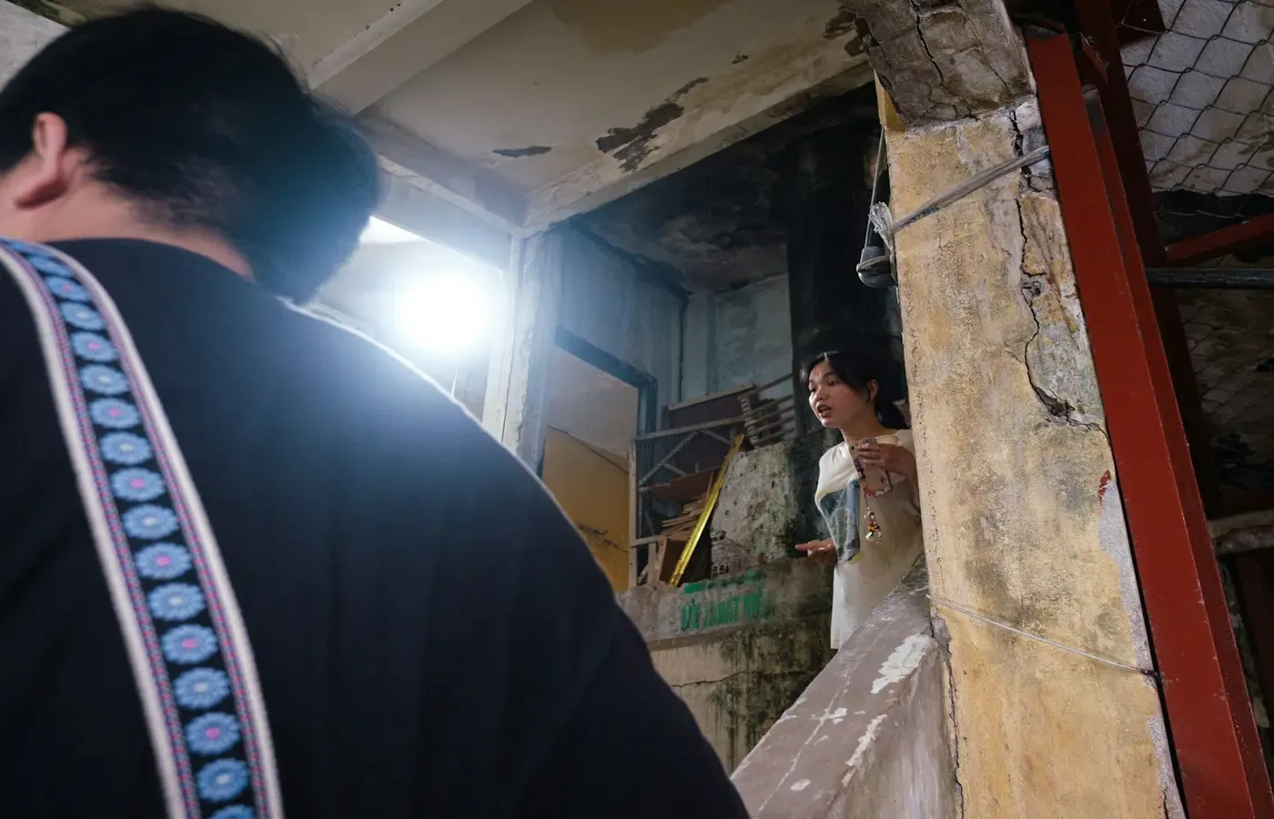 Man observes woman in white dress in a rundown interior